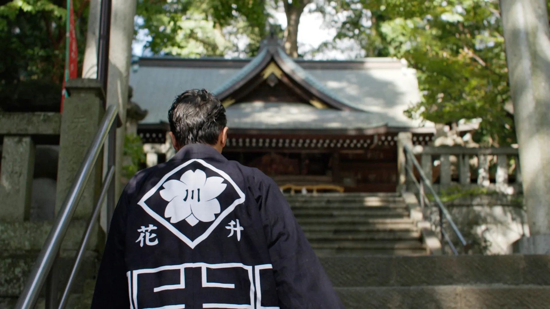 神社の石段の前に立つ花升の宮大工棟梁の後ろ姿